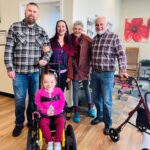 Emma is smiling in her wheelchair with her family and donors.