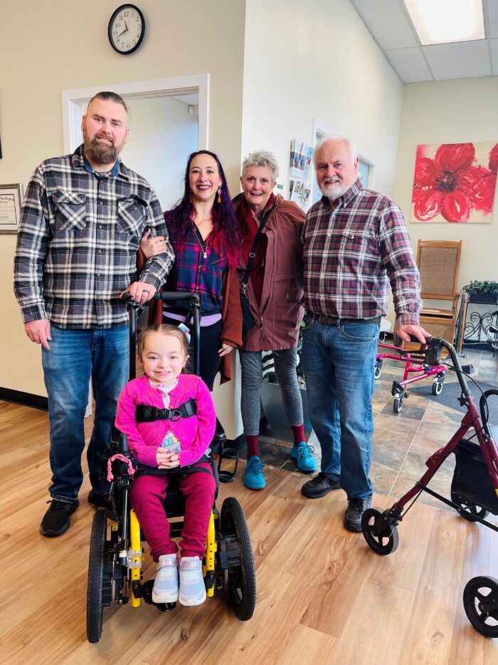 Emma is smiling in her wheelchair with her family and donors.